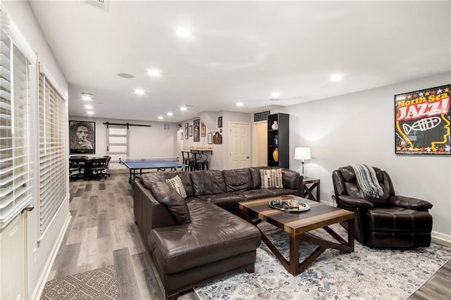 living area with recessed lighting, wood finished floors, baseboards, and a barn door