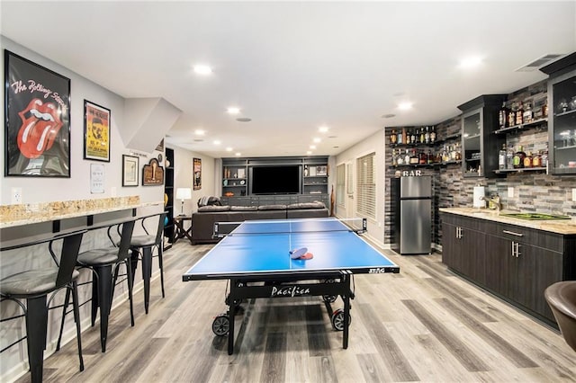 rec room with light wood-style floors, recessed lighting, indoor bar, and visible vents