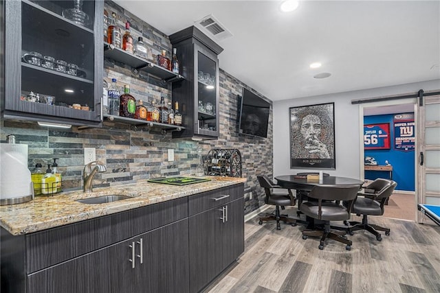 bar with a barn door, visible vents, wet bar, light wood-type flooring, and a sink