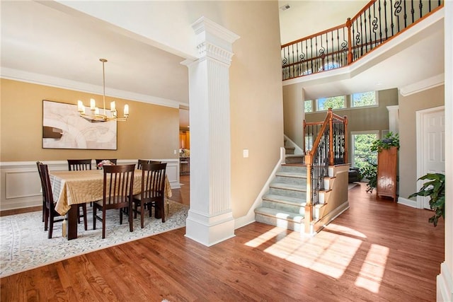 dining area featuring decorative columns, stairway, ornamental molding, wood finished floors, and a chandelier