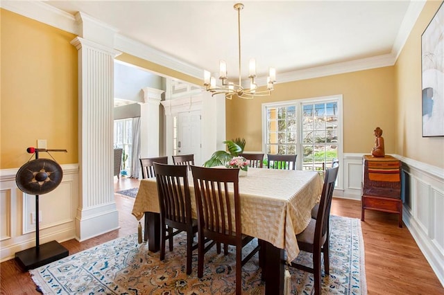 dining area featuring a notable chandelier, plenty of natural light, ornate columns, and wood finished floors