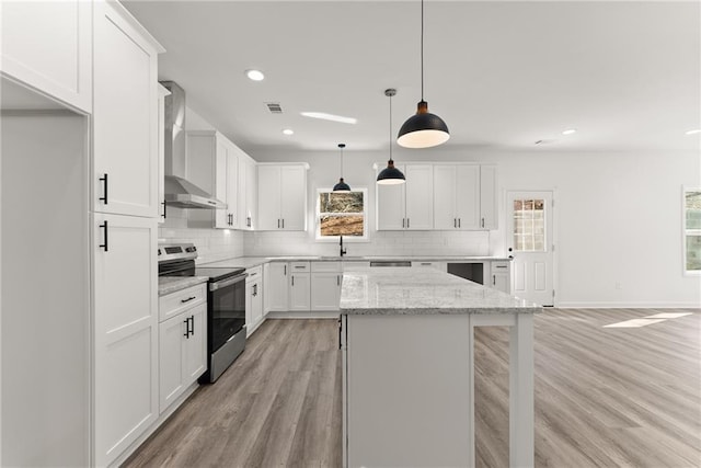 kitchen with decorative light fixtures, stainless steel electric range, wall chimney exhaust hood, white cabinets, and light stone counters