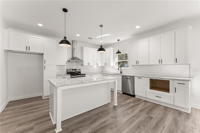 kitchen with wall chimney range hood, pendant lighting, a kitchen island, stainless steel appliances, and white cabinets