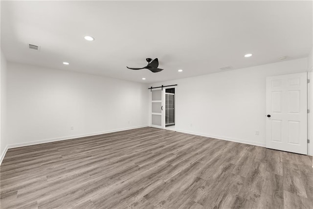 unfurnished room featuring ceiling fan, a barn door, and light hardwood / wood-style floors