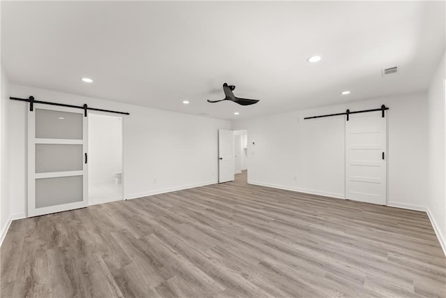 unfurnished room with ceiling fan, a barn door, and light hardwood / wood-style flooring