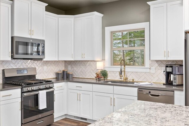kitchen featuring stainless steel appliances, a sink, tasteful backsplash, and white cabinets