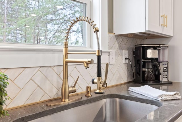 kitchen view of tasteful backsplash, white cabinets, dark stone counters, and a sink