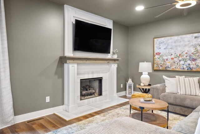 living area featuring a ceiling fan, wood finished floors, baseboards, and a fireplace