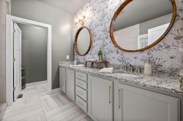 full bath featuring wallpapered walls, double vanity, and baseboards