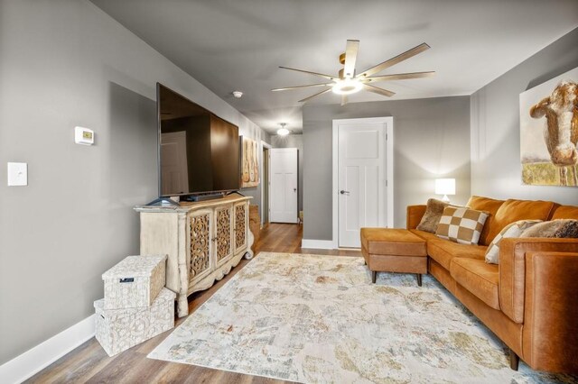 living room with ceiling fan, baseboards, and wood finished floors