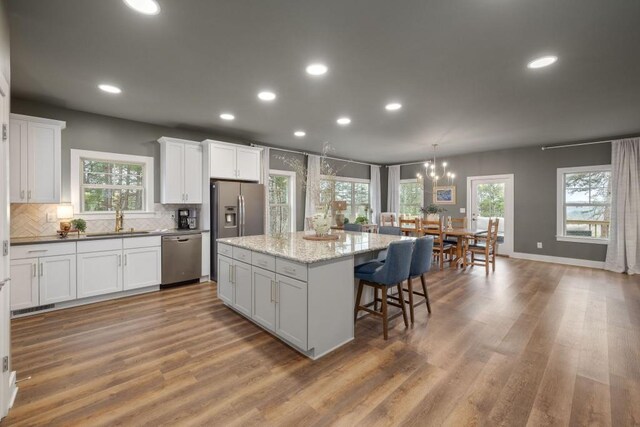 kitchen with appliances with stainless steel finishes, a sink, white cabinetry, a kitchen island, and backsplash