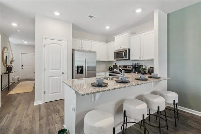 kitchen with sink, appliances with stainless steel finishes, white cabinetry, light stone countertops, and a kitchen bar