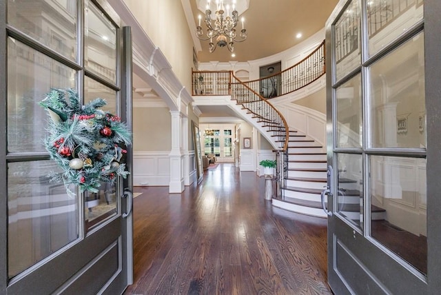 entrance foyer with ornate columns, dark wood-type flooring, a notable chandelier, a towering ceiling, and ornamental molding