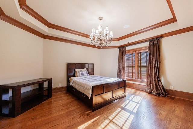 bedroom featuring a raised ceiling, wood-type flooring, ornamental molding, and an inviting chandelier