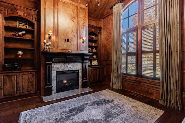 unfurnished living room featuring built in shelves, dark hardwood / wood-style flooring, vaulted ceiling, and a wealth of natural light