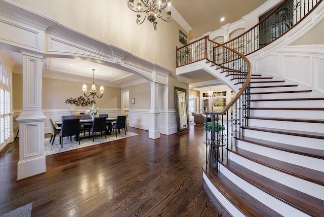 entrance foyer featuring a towering ceiling, ornate columns, ornamental molding, dark wood-type flooring, and a chandelier