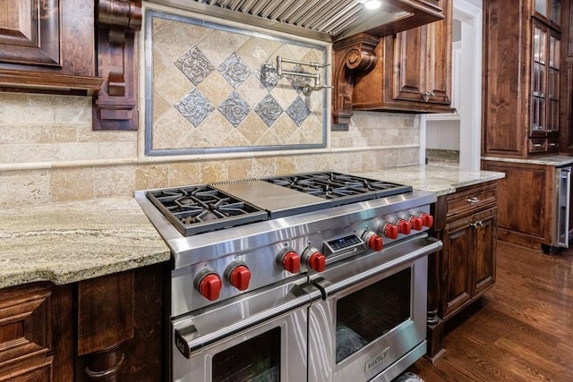 kitchen featuring light stone countertops, tasteful backsplash, dark brown cabinets, dark wood-type flooring, and range with two ovens