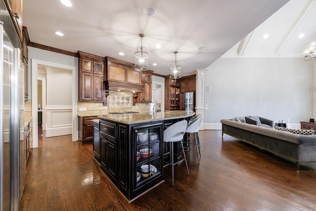 kitchen featuring light stone countertops, dark wood-type flooring, a kitchen breakfast bar, an island with sink, and decorative backsplash