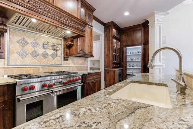 kitchen with decorative backsplash, light stone countertops, premium range hood, sink, and range with two ovens