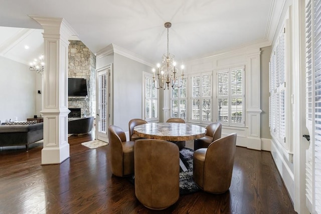 dining room with a stone fireplace, crown molding, a notable chandelier, dark hardwood / wood-style flooring, and decorative columns