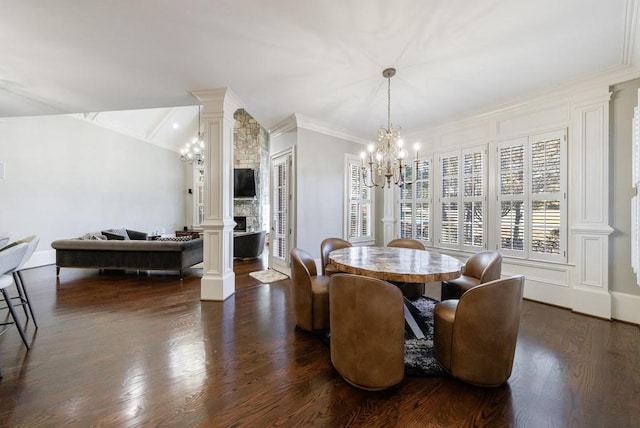 dining room featuring dark hardwood / wood-style flooring, ornate columns, ornamental molding, an inviting chandelier, and a fireplace