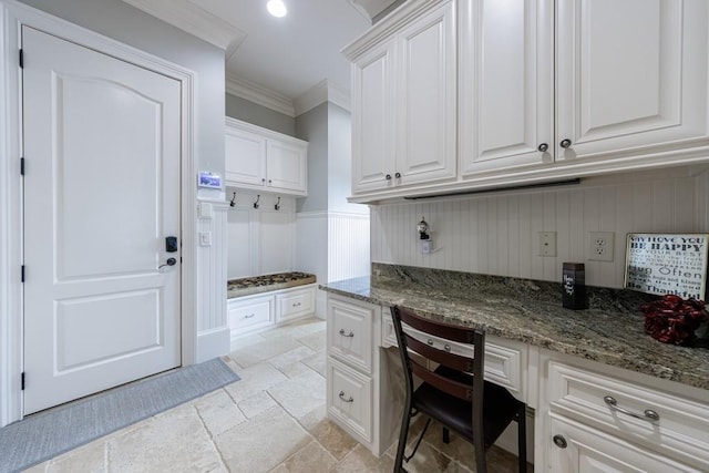 interior space with dark stone countertops, white cabinetry, built in desk, and ornamental molding