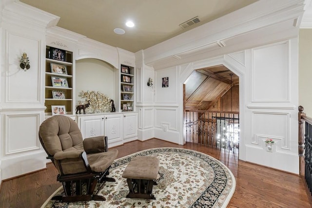 sitting room featuring built in shelves, hardwood / wood-style flooring, and crown molding