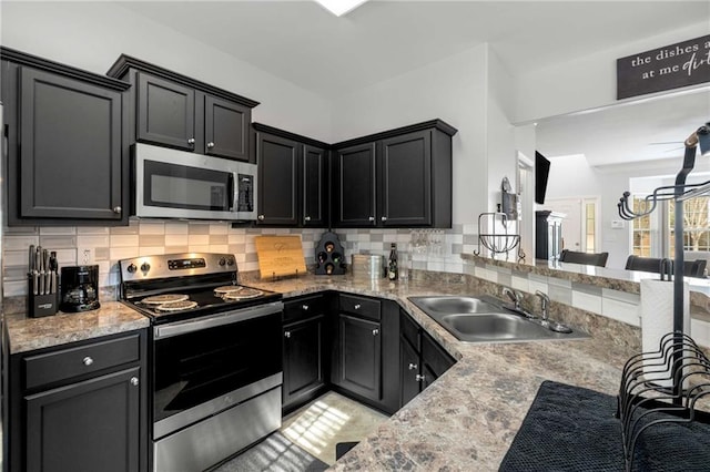 kitchen featuring sink, appliances with stainless steel finishes, kitchen peninsula, light stone countertops, and backsplash