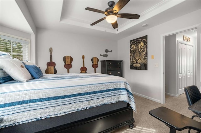 carpeted bedroom with ceiling fan and a tray ceiling