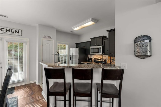 kitchen with light stone counters, a kitchen breakfast bar, kitchen peninsula, stainless steel appliances, and backsplash