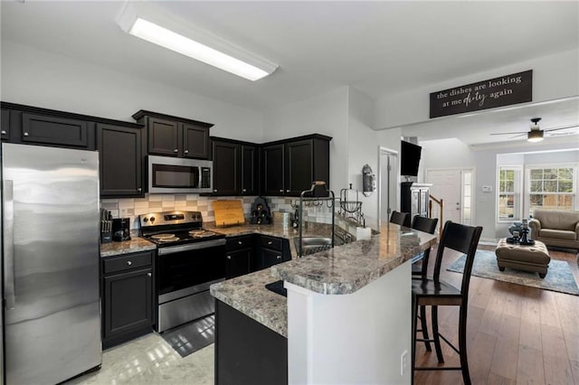 kitchen with a breakfast bar area, tasteful backsplash, light stone counters, light wood-type flooring, and appliances with stainless steel finishes