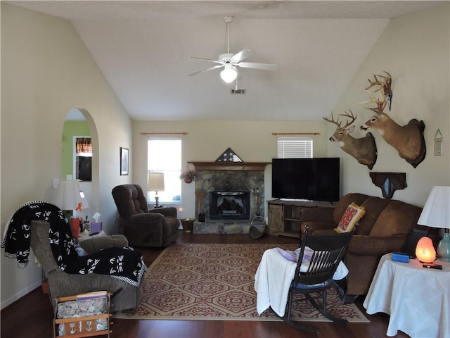 living room featuring ceiling fan, high vaulted ceiling, dark wood-type flooring, and a stone fireplace