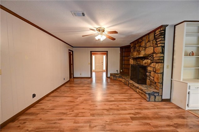 unfurnished living room featuring a stone fireplace, a textured ceiling, ceiling fan, light wood-type flooring, and built in features