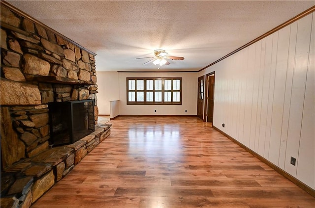 unfurnished living room with a stone fireplace, a textured ceiling, light wood-type flooring, and crown molding