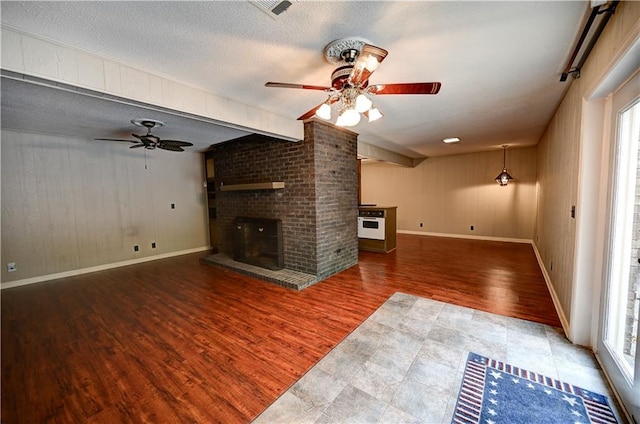 unfurnished living room featuring a textured ceiling, a brick fireplace, hardwood / wood-style flooring, and ceiling fan