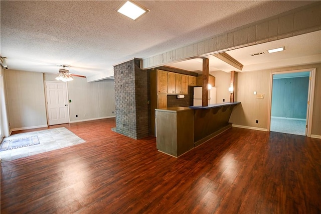 kitchen with a breakfast bar, kitchen peninsula, ceiling fan, a textured ceiling, and dark wood-type flooring