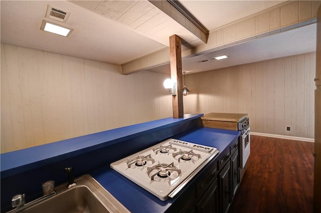 interior space with dark hardwood / wood-style flooring, white gas stovetop, wooden walls, and sink