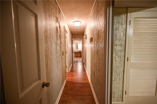 hall featuring dark wood-type flooring, wooden walls, and a textured ceiling