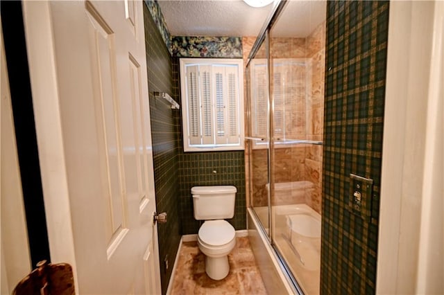 bathroom featuring tile patterned floors, toilet, tile walls, bath / shower combo with glass door, and a textured ceiling