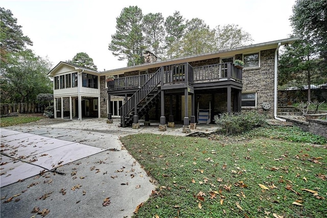 back of property with a wooden deck, a lawn, a patio, and a sunroom