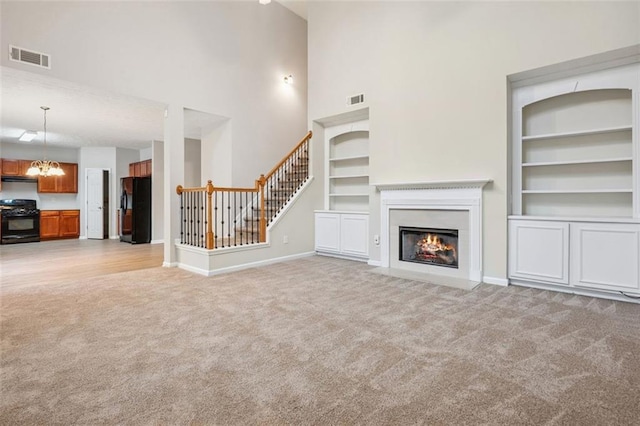 2040 Village Green Dr, Fairburn, GA 30213 - unfurnished living room with light carpet, built in shelves, a towering ceiling, a chandelier, and stairs