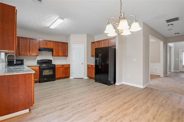 2040 Village Green Dr, Fairburn, GA 30213 - kitchen with black appliances, under cabinet range hood, light wood finished floors, brown cabinets, and a textured ceiling