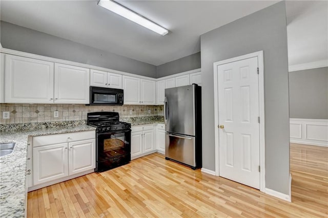 kitchen with white cabinets, light stone counters, light wood-type flooring, decorative backsplash, and black appliances