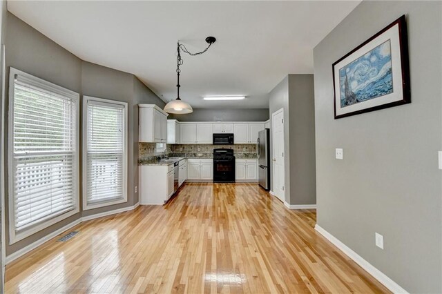 kitchen featuring light wood-style flooring, tasteful backsplash, freestanding refrigerator, stove, and black microwave