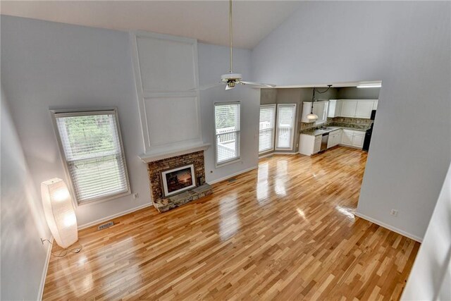 unfurnished living room with light wood-style floors, a healthy amount of sunlight, a ceiling fan, and high vaulted ceiling