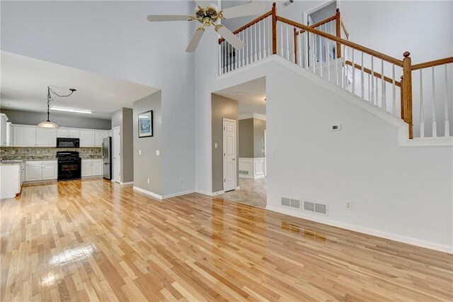 unfurnished living room with light wood-style floors, ceiling fan, baseboards, a high ceiling, and visible vents