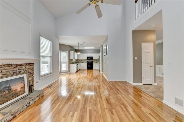 unfurnished living room featuring light wood finished floors, visible vents, a ceiling fan, a stone fireplace, and high vaulted ceiling