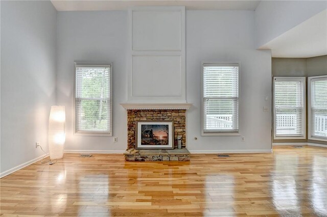 unfurnished living room with wood finished floors, baseboards, and a stone fireplace
