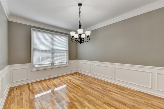 unfurnished room featuring crown molding, a notable chandelier, a wainscoted wall, and light wood-style floors