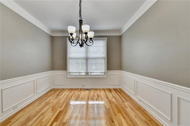 unfurnished dining area featuring an inviting chandelier, ornamental molding, light wood-style floors, a decorative wall, and wainscoting